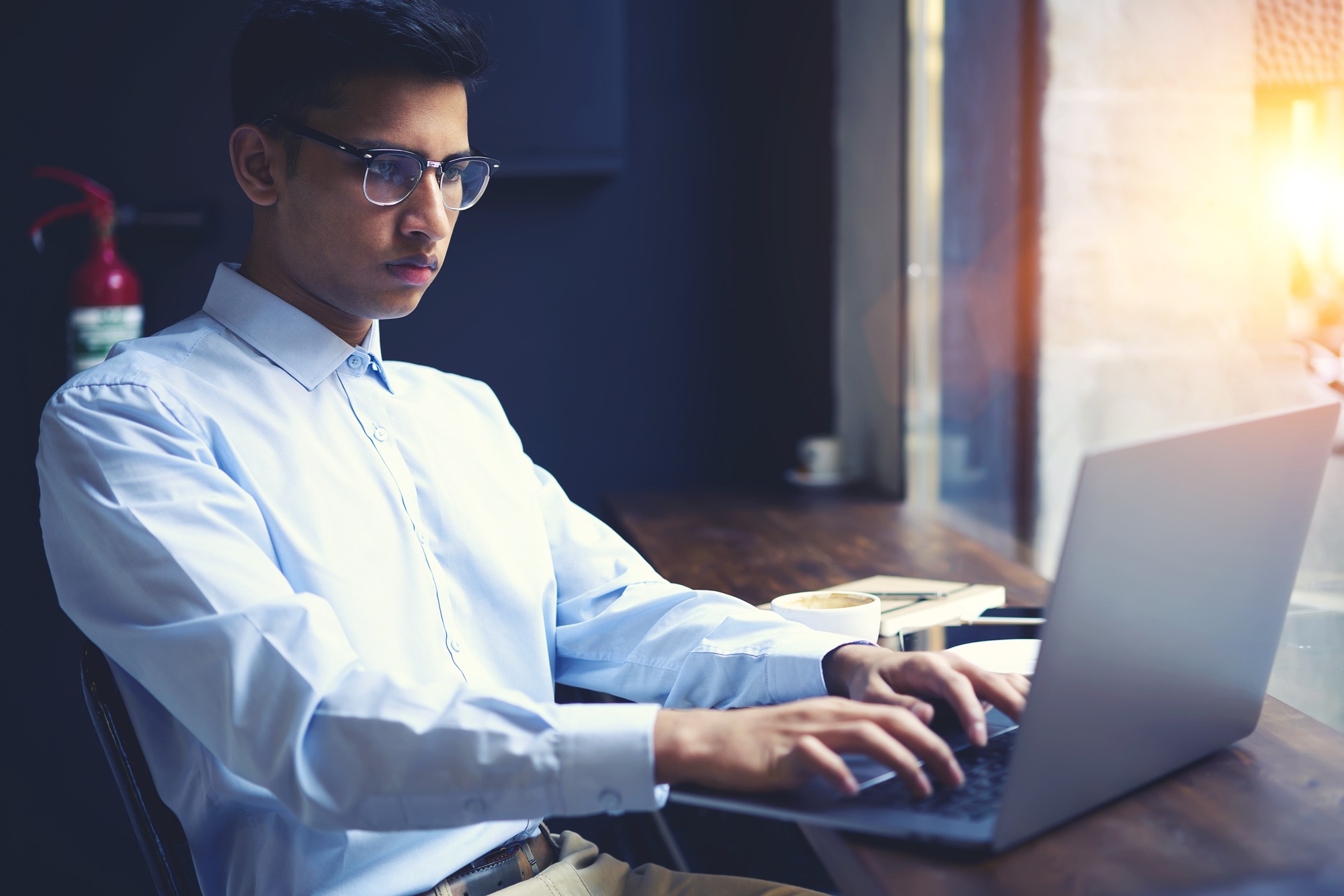 Concentrated handsome well-dressed male international student typing on laptop computer